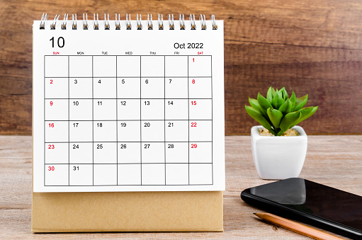 Asian man marks important date on desk calendar with pen at work station in office