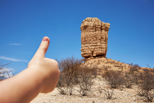 A toddler raises his thumb and compares it to the Vingerklip or Fingerklip under a blue sky in Namibia, Photographed in high resolution with copy space