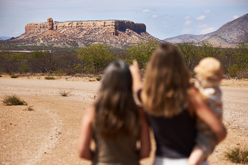 Two women and a child point to the Vingerklip or Fingerklip under a blue sky in Namibia, photographed in high resolution with copy space