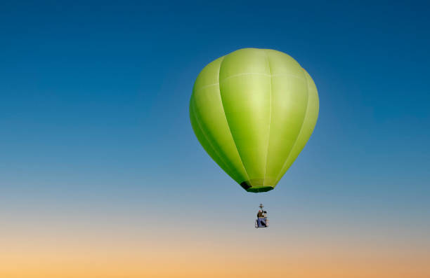 Green hot air balloon in flight on blue sky