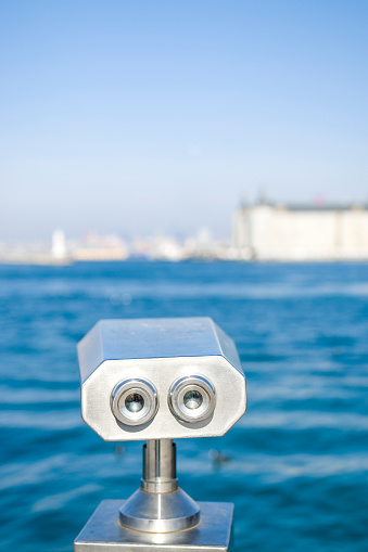 Public binoculars on the seaside promenade overlooking a distant city.