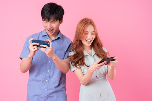 Young Asian couple using smartphone on pink background