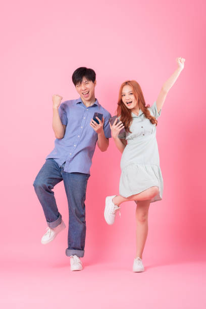 istock Young Asian couple using smartphone on pink background 1370902285