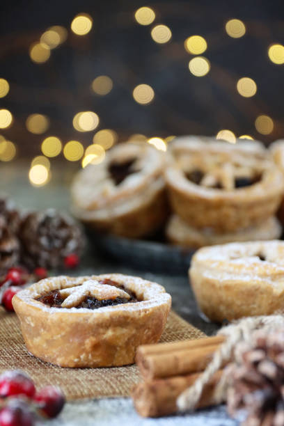 istock Close-up image of stack of homemade mince pies dusted with icing sugar, cinnamon bundle, hessian, red berries, pine cones, blurred illuminated fairy lights background, focus on foreground 1370904859