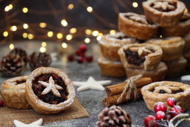 istock Image of stack of cooked, homemade mince pies dusted with icing sugar, tart with missing bite, cinnamon bundle, red berries, red berries, blurred white fairy lights background, focus on foreground 1370904927