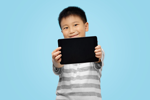 Happy kid holding and showing tablet, weaing tshirt on blue background