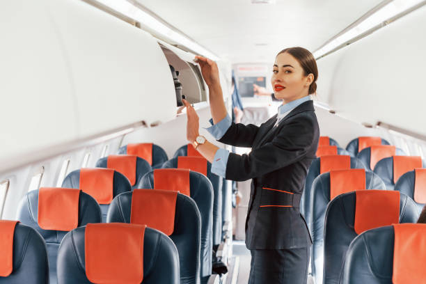 Young stewardess that is in formal black clothes is standing indoors in the plane Young stewardess that is in formal black clothes is standing indoors in the plane. crew stock pictures, royalty-free photos & images