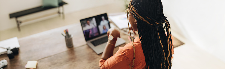 Female designer attending a virtual meeting with her clients. Young female freelancer using a laptop for a video call. Creative young woman working on a new project in her home office.