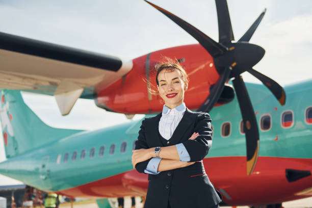 istock At daytime. Young stewardess that is in formal black clothes is standing outdoors near plane 1370907077