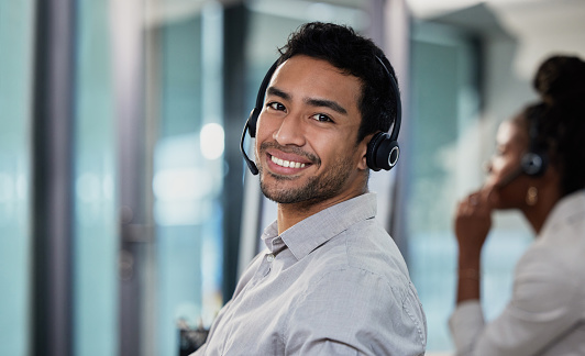 Shot of a handsome young customer service agent sitting in the office and wearing a headset