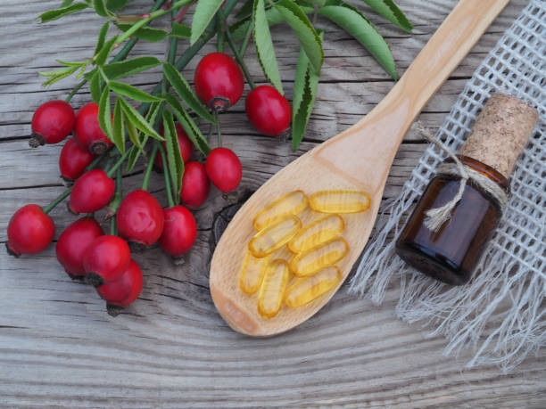 Wild rose branches with ripe berries, yellow capsules and a bottle of cosmetic oil, syrup on a wooden table, closeup, top view. Natural useful plant rosehip with vitamin C for strengthen the immune system ramas de rosas silvestres con bayas maduras, cápsulas amarillas y una botella de aceite cosmético, jarabe sobre una mesa de madera, primer plano, vista superior. planta natural útil rosa mosqueta con vitamina c para fortalecer el sistema inmunológico
