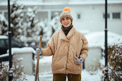 Youbg woman posing after cleaning pathway to her home, on a snowy day