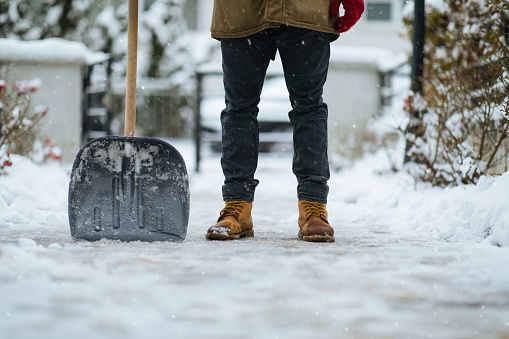 Shovel and boots of a man after cleaning path from snow in yard
