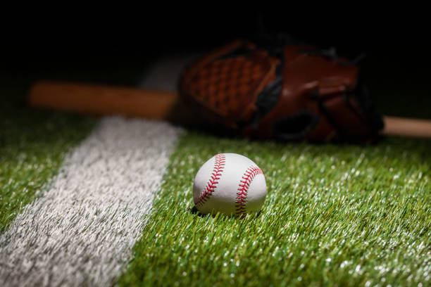 istock Low angle view of baseball on grass field with stripe and defocused mitt and bat 1370911498