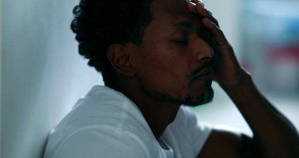 istock Black man feeling stress, african descent sitting on floor rubbing face with hand feeling worry and preoccupation, mental illness concept 1370914247