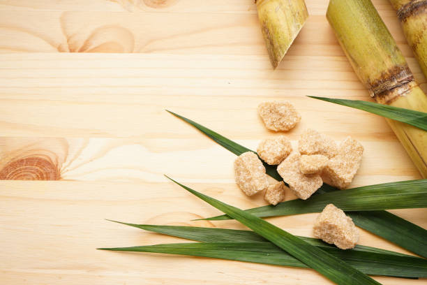 Sugarcane, green leaf and brown sugar on a wooden background with space for text. Top view.