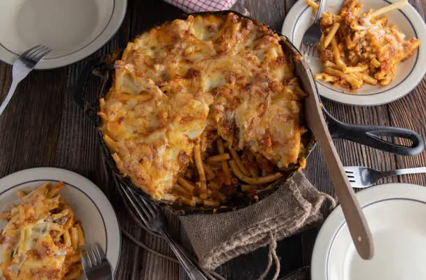 Homemade fresh cooked italian pasta casserole with bolognese sauce, bechamel sauce and a delicious cheese crust. Baked in a cast iron pan and served on wooden table. Overhead view and ready to eat