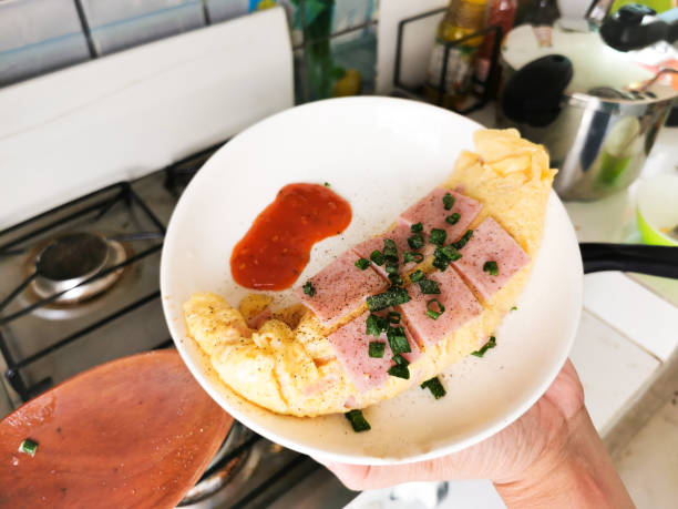 Delicious omelet on top with square ham and sprinkled with sliced ​​cilantro on a white plate.