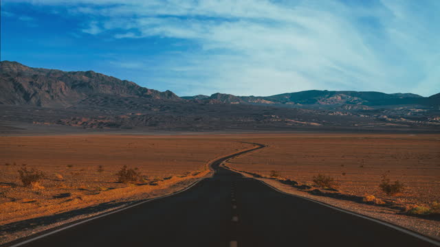 Death Valley National Park Cinemagraph / seamless video loop time lapse of a lonely straight highway road and clouds moving along the blue sky above the dry, hot, empty and remote desert of Nevada and California, United States of America.