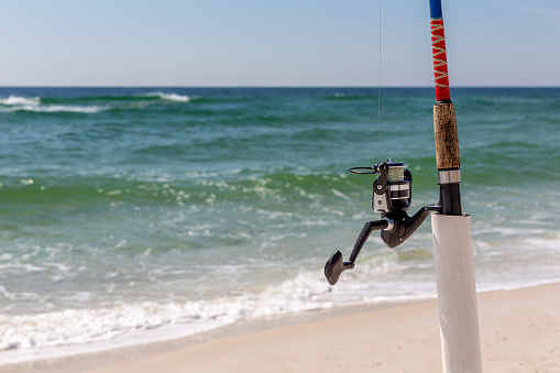 Surf fishing pole in a holder at the shore.  Close up view with copy space if needed.  Concepts could include fishing, travel, relaxation, leisure.