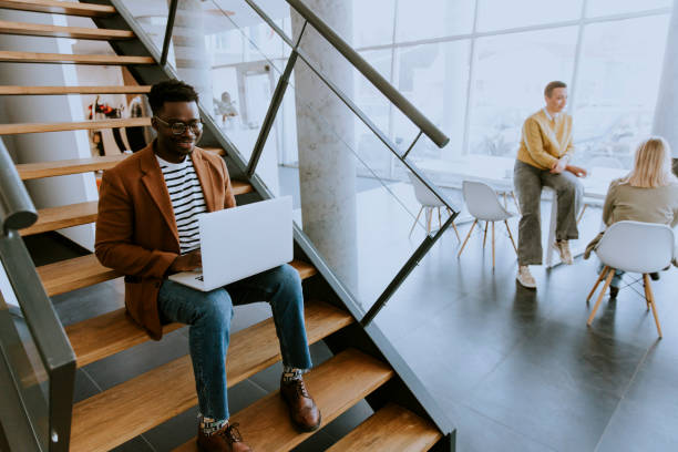 istock Young African American business man working on laptop computer while sitting on a office stairs 1370930014