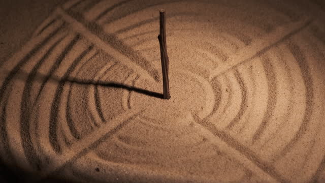 Stylized as a sundial. Rod, sunbeam and circles in the sand