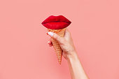 Ice cream waffle cone with red lips inside in a female hand. Contemporary art. Modern design