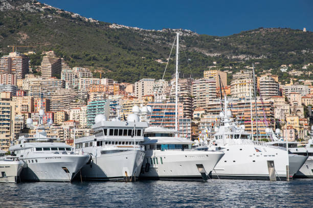 a lot of huge yachts are in port of monaco at sunny day, megayachts are moored in marina, is a yacht show, monte carlo, real estate housing is on background, glossy board of the motor boat - monaco società reale 個照片及圖片檔