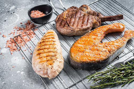 Set of bbq grilled meat steaks salmon, beef and turkey on a grill. Gray background. Top view.