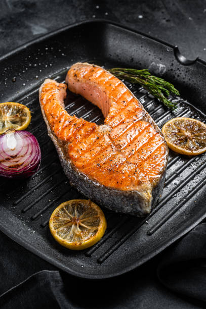 istock Salmon Fish Steak grilled on a grill pan with herbs. Black background. Top view 1370937142