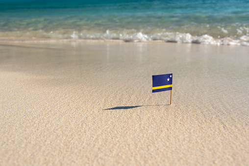 Small paper flag of curaçao on a white sandy beach with a crystal clear ocean.