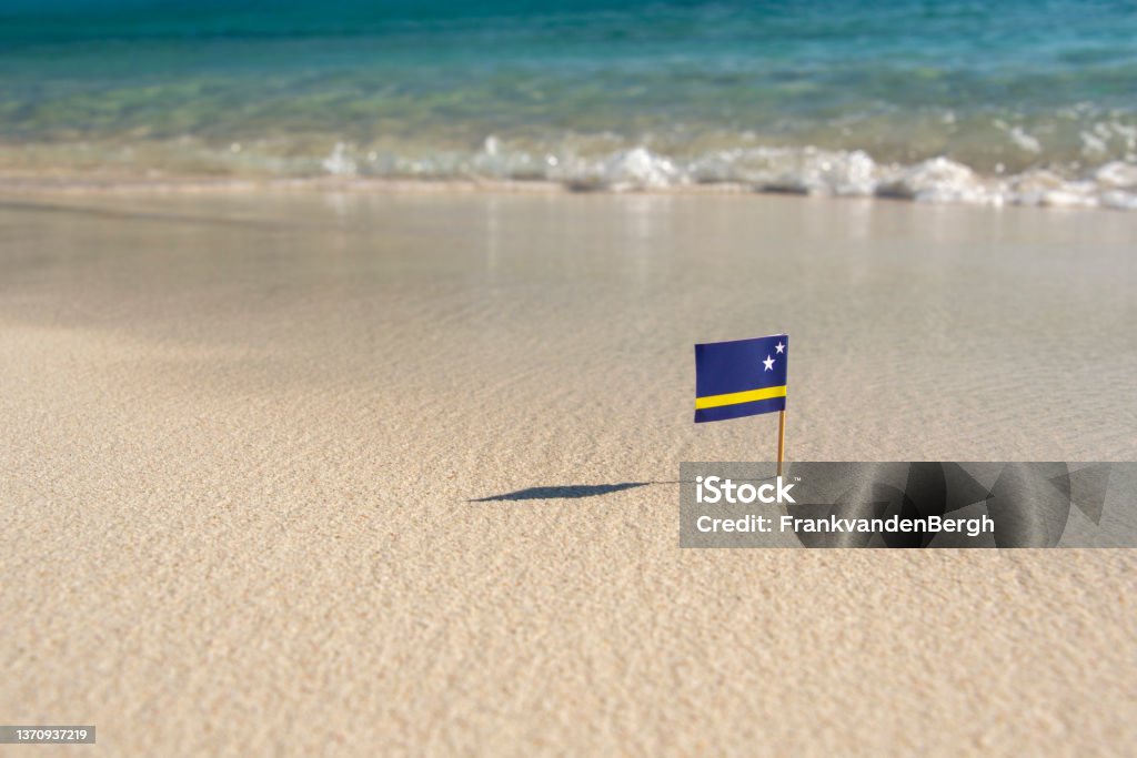 Flag on the beach Small paper flag of curaçao on a white sandy beach with a crystal clear ocean. Curaçao Stock Photo