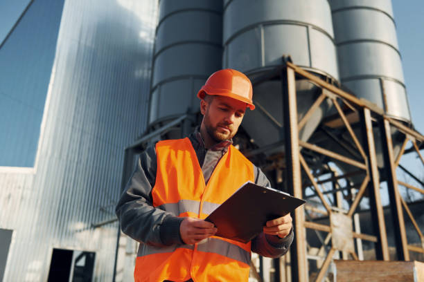 istock Holding notepad in hands. Construction worker in uniform is outdoors near the factory 1370938111