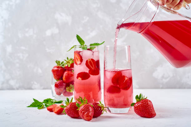 Woman pours strawberry lemonade in glass. Cocktail with strawberry, ice and mint in glasses on white concrete background, copy space. Refreshing summer berry drink stock photo