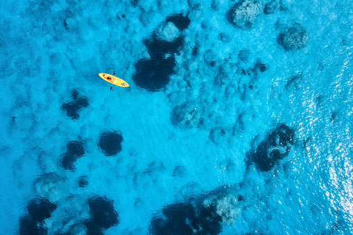 Aerial view of yellow kayak in blue sea at sunset in summer. Man on floating canoe in clear azure water. Lefkada island, Greece. Tropical landscape. Sup board. Active travel. Top view. Vacations