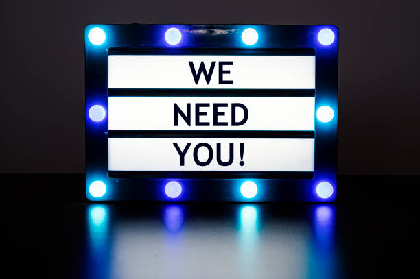 istock Lightbox with blue lights in dark room with words - we need you! 1370941238