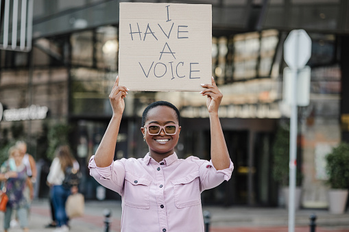 Young short hair woman standing on the street and holding carboard sign I have a voice