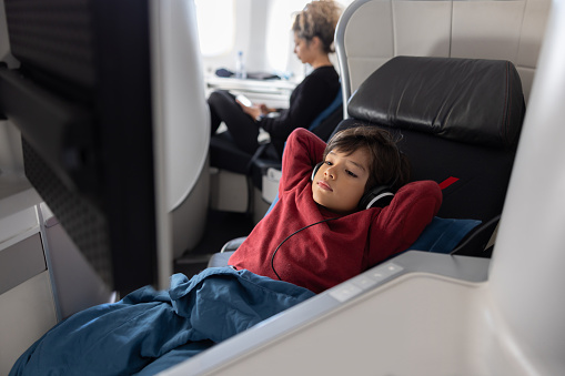 Latin American boy traveling by plane in business class and watching a movie using headphones