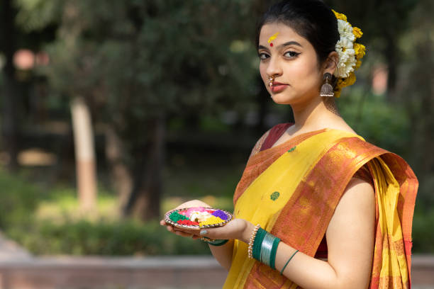 Beautiful young woman or girl in yellow saree posing with color or colour or gulal or abeer or Holi powder in a decorated plate to celebrate holi festival of colors stock photo
