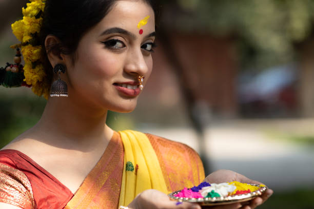 Young and beautiful girl or woman in yellow saree with a plate of color or colour or gulal or abeer or Holi powder in a decorated plate to celebrate holi festival of colors stock photo