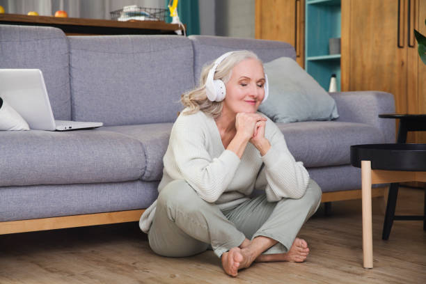 elderly woman in headphones listens to music  at home in the evening. seniors llifestyle. meditation. Audio healing. stock photo