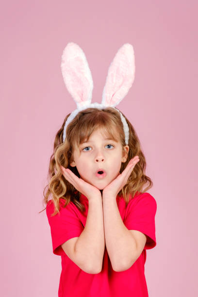 istock Surprised little girl with bunny ears touching face and smiling in studio 1370967652