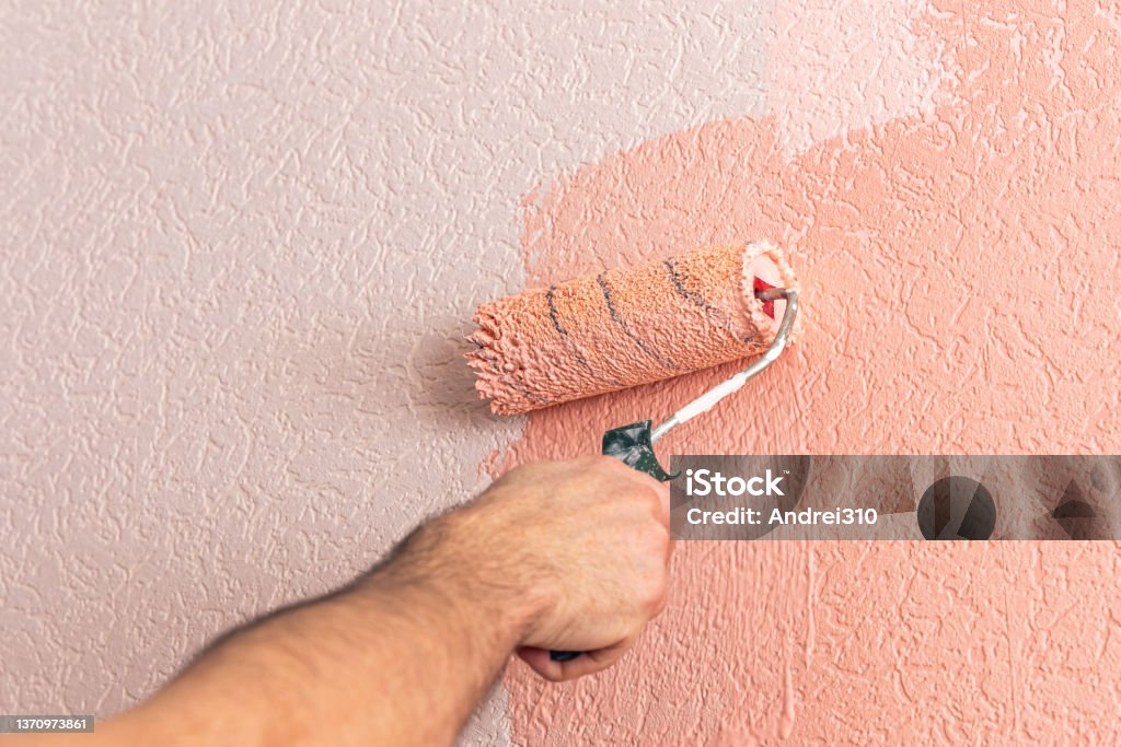 Man's hand paints the wall with a paint roller in pink .Man's hand paints the wall with a paint roller in pink. Interior Designer Stock Photo