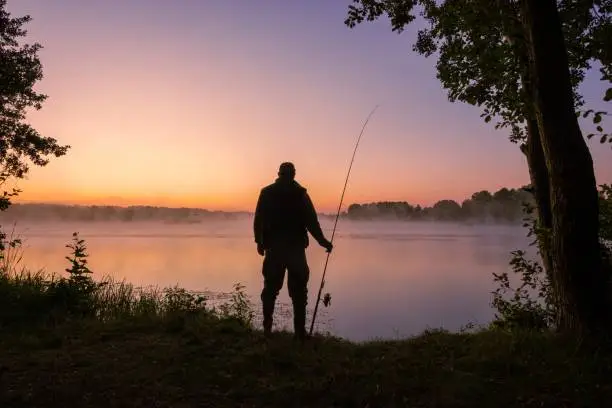 Silhouette of angler with fishing rod during sunrise