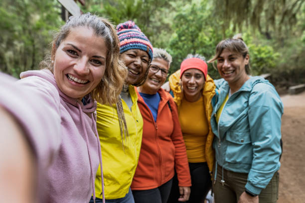 grupo de mujeres con diferentes edades y etnias divirtiéndose tomándose selfie mientras caminan por un bosque brumoso - concepto de gente de aventura y viaje - public land fotografías e imágenes de stock