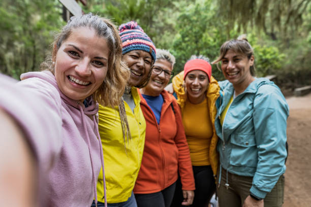 Group of women with different ages and ethnicities having fun taking selfie while walking in foggy forest - Adventure and travel people concept stock photo