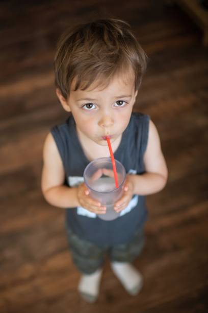 Caucasian Little boy drinking holding a glass of water using a plastic straw from above