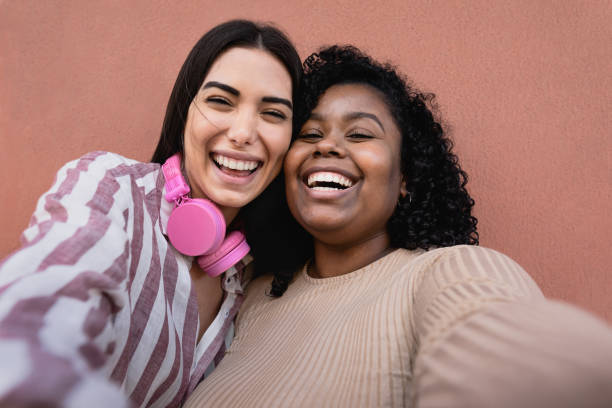 Happy Hispanic friends having fun taking selfie with mobile smartphone outdoor - Technology and social media concept stock photo