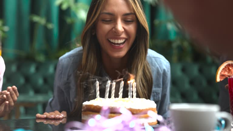 Close up of beautiful woman celebrating her birthday blowing out the candles on cake looking very happy and with a toothy smile