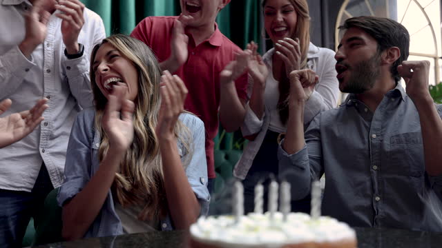 Close up of Latin American people celebrating the birthday of their female friend while she blows out the candles on cake at a bar